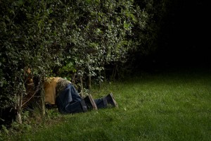 Boy (8-9) crawling into bushes in dark yard at night, side view, low section